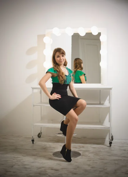 Frau sitzt auf Stuhl in Umkleidekabine mit Spiegel mit Glühbirnen — Stockfoto