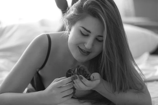 Monocromático retrato bonito mulher deitada na cama e segurando rosa — Fotografia de Stock