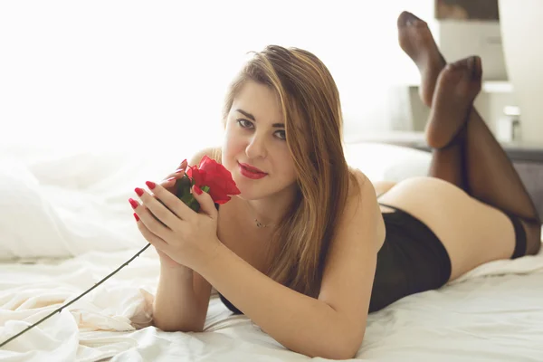 Belle femme en lingerie couchée au lit et sentant rose rouge — Photo