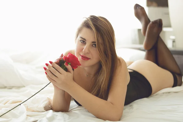 Mooie vrouw in lingerie in bed liggen en ruiken rode roos — Stockfoto