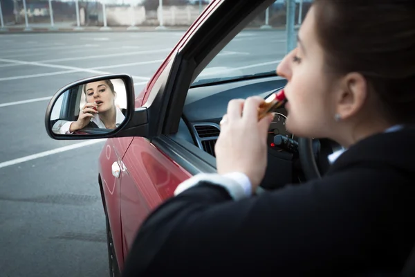 Деловая женщина, сидящая в машине и нанося помаду — стоковое фото