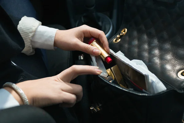 Woman sitting in car and taking lipstick out of handbag — Stock Photo, Image