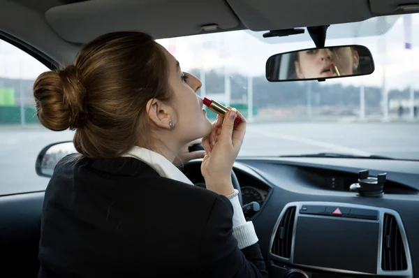 Businesswoman looking in mirror at car and applying cosmetics — Stock Photo, Image
