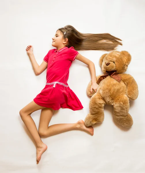 Sonriente chica acostada en el suelo y fingiendo correr rápido con Ted — Foto de Stock