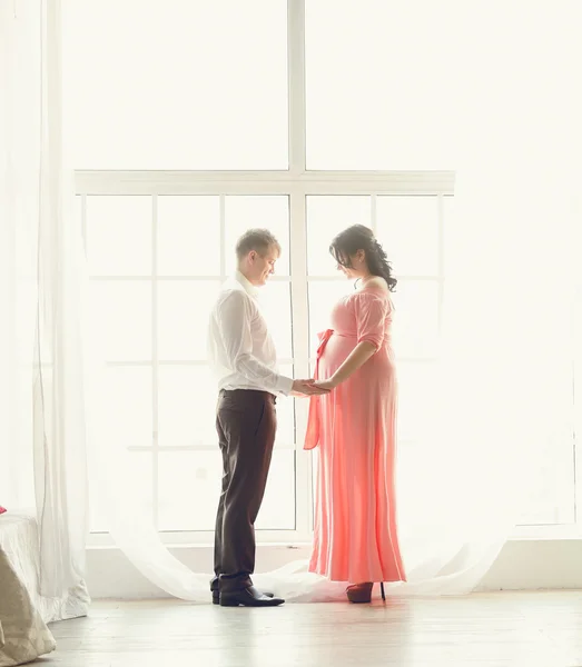 Toned photo of beautiful pregnant couple holding hands at window — Stock Photo, Image