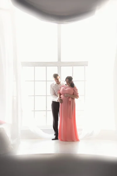 Silhouette photo of pregnant couple embracing against big window — Stock Photo, Image
