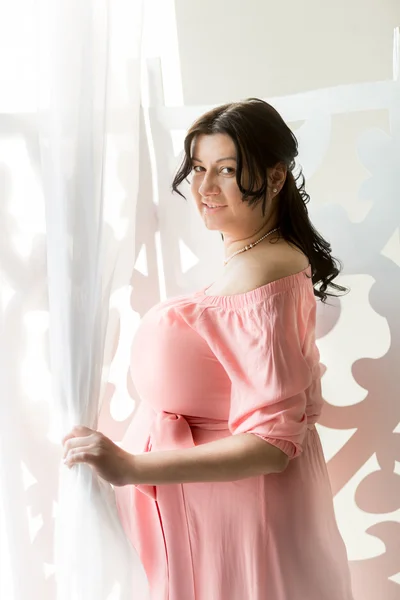 Portretul unei femei însărcinate frumoase care deschide perdele pe fereastră — Fotografie, imagine de stoc