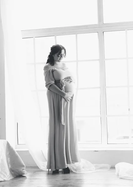 Schwarz-Weiß-Aufnahme einer schwangeren Frau, die vor einem großen Fenster posiert — Stockfoto