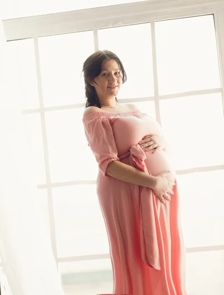 Toned shot of pregnant brunette woman posing against big window — Stock Photo, Image