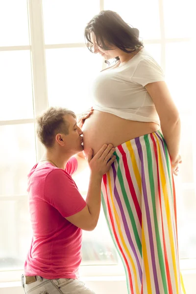 Homem ajoelhado beijando barriga da esposa grávida na sala de estar — Fotografia de Stock