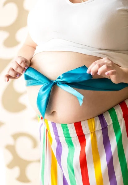 Nahaufnahme einer niedlichen Schwangeren, die sich eine Schleife auf den Bauch bindet — Stockfoto