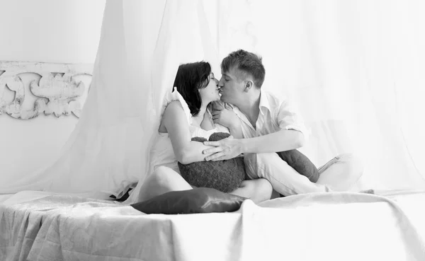 Black and white shot of happy pregnant couple kissing on bed — Stock Photo, Image