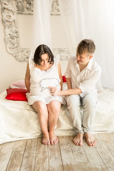 Coppia incinta seduta sul letto e tenendo copia segno spazio su ab — Foto Stock