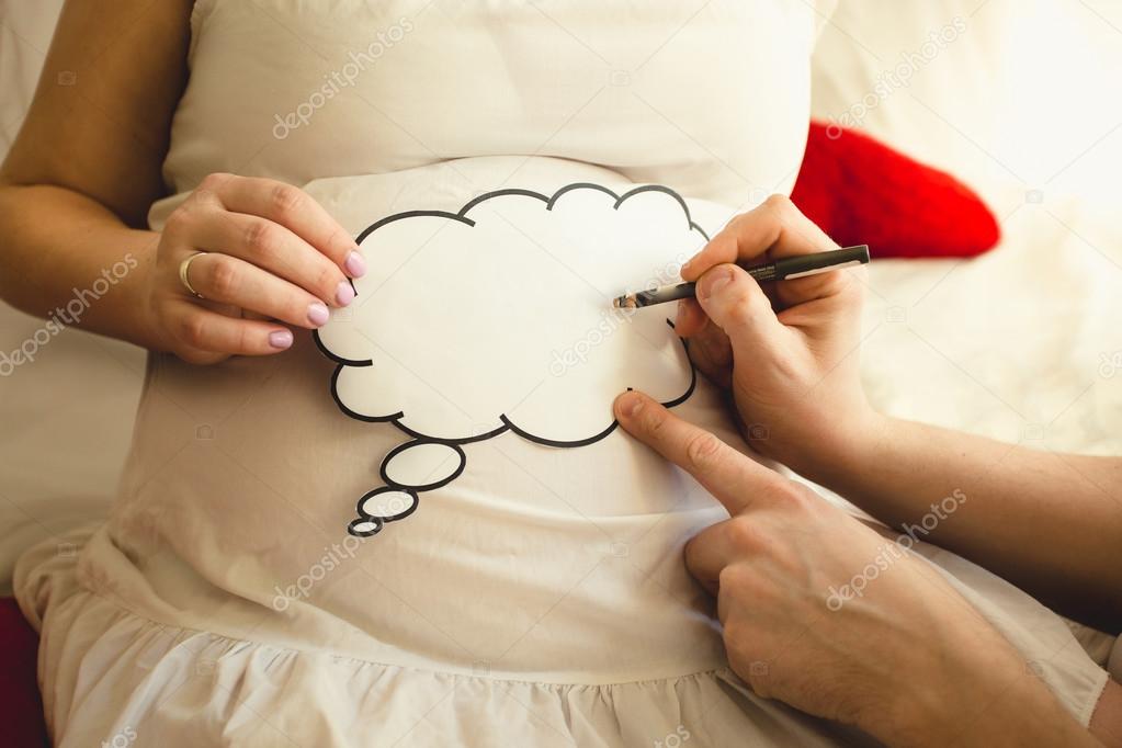 Closeup of photo of man writing on sign on wife's pregnant abdom