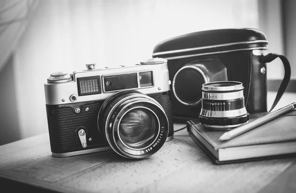 Black and white closeup photo of old camera and notebook on desk — Stock Photo, Image