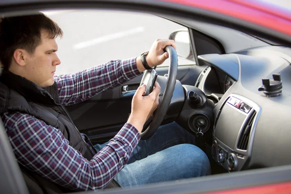 Young man typing message while driving a car — Stock Photo, Image