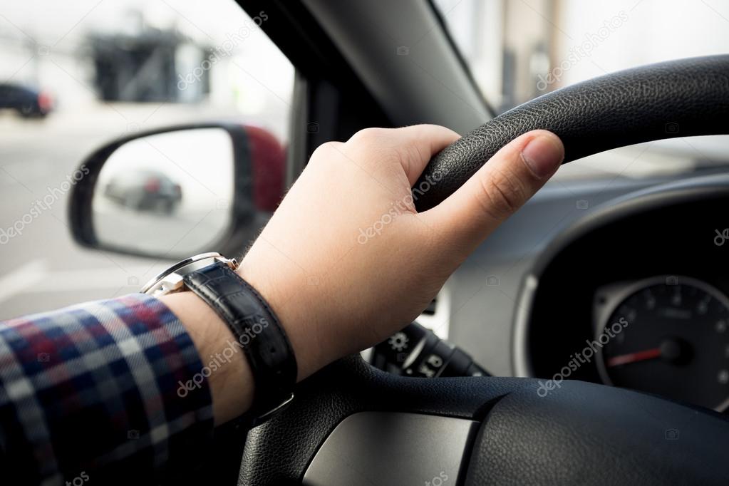 Closeup of male hand in watches holding car steering wheel