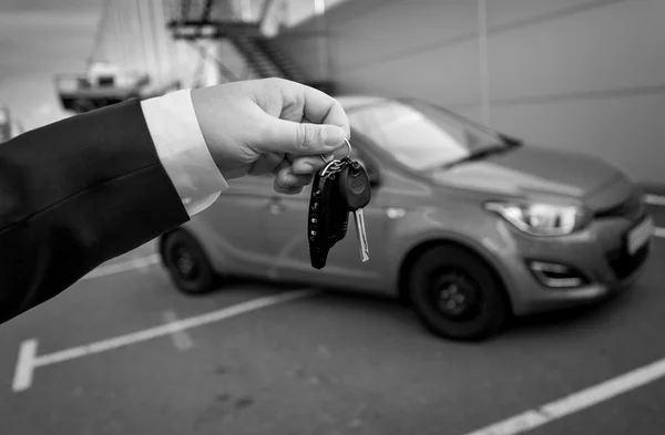 Schwarz-Weiß-Foto eines Mannes im Anzug, der Autoschlüssel gegen den Kopf hält — Stockfoto