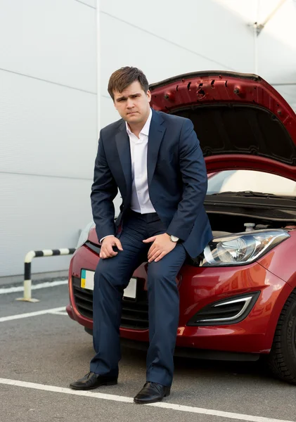 Man in suit sitting on broken car with open hood — Stock Photo, Image