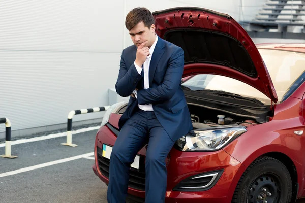 Upset businessman sitting on bonnet of broken car — Stock Photo, Image