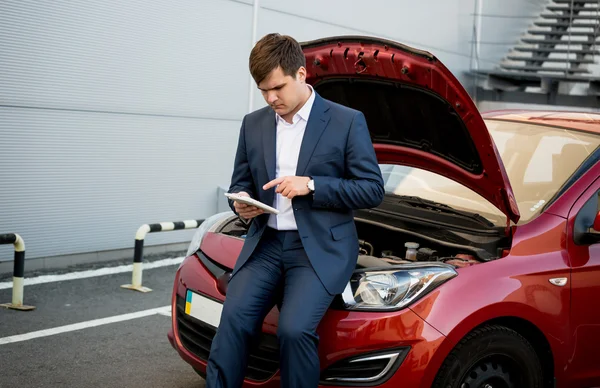 Geschäftsmann sitzt auf Motorhaube des kaputten Autos und sucht, wie man f — Stockfoto