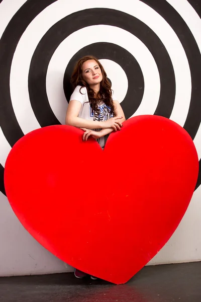 Smiling woman holding big red heart in studio — Stock Photo, Image