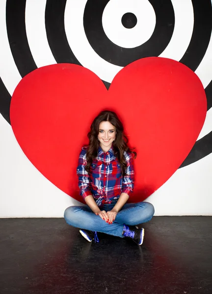 Joven mujer sonriente sentada en el suelo con gran corazón rojo — Foto de Stock