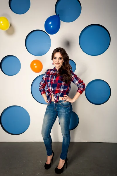 Smiling girl in jeans posing against background with balloons — Stock Photo, Image