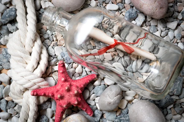 Carta en botella sobre piedras con estrella de mar y nudo marino —  Fotos de Stock