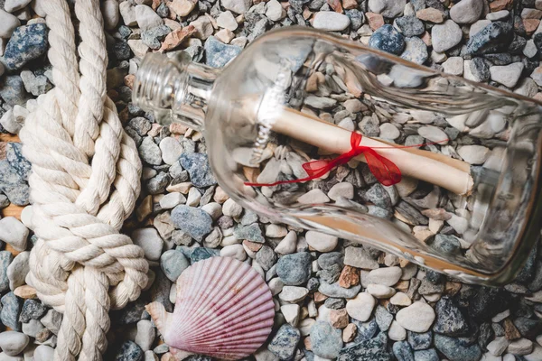 Letter in bottle lying on seashore with rope and seashells — Stock Photo, Image