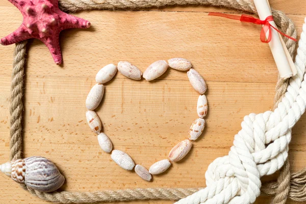 Coeur fait de coquillages avec bordure de cordes et de nœuds sur les planches — Photo