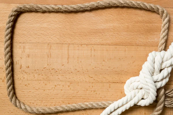 Closeup of frame made of rope and marine knot over wooden desk — Stock Photo, Image