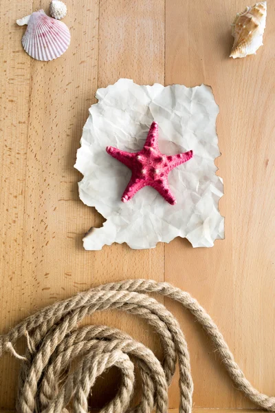 Red starfish lying on piece of old paper on wooden planks — Stock Photo, Image