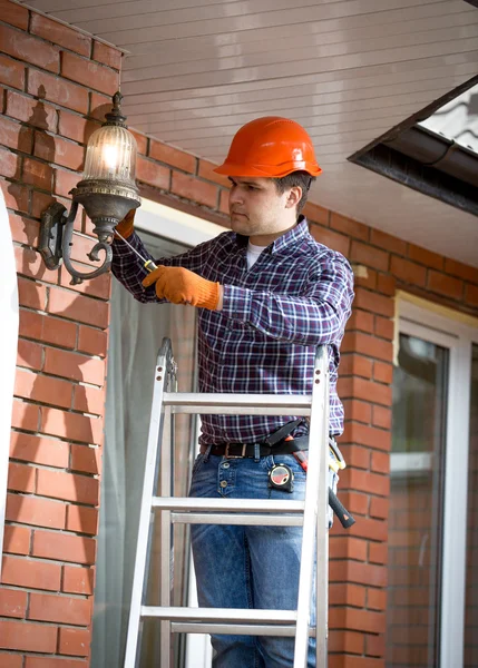 Elektriker steht auf Leiter und wechselt Außenlampe — Stockfoto