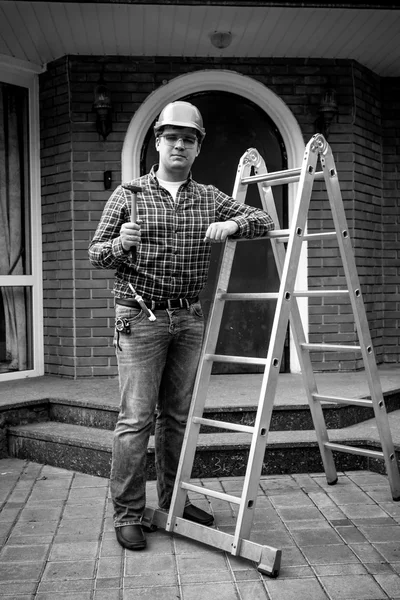 Black and white shot of worker posing with tools at metal ladder — Stock Photo, Image