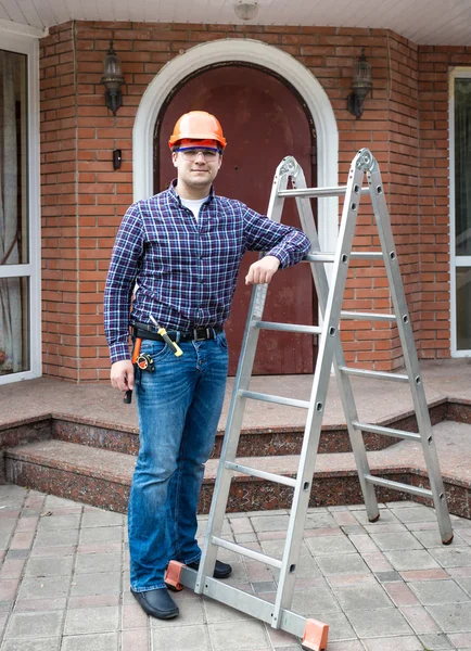 Mannelijke bouwer in helm poseren met ladder tegen huis ingang — Stockfoto