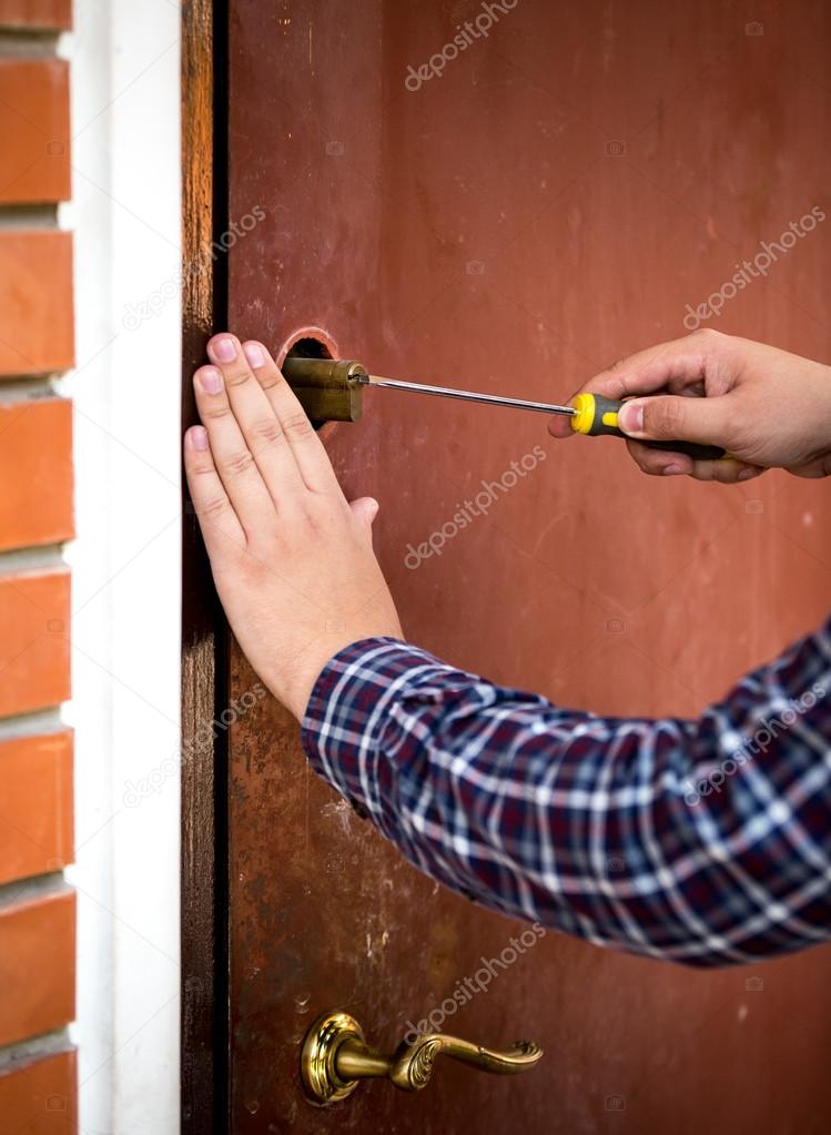 Closeup of carpenter fixing door lock with screwdriver