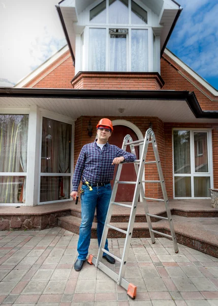 Улыбающийся рабочий позирует против красивого недавно построенного дома — стоковое фото