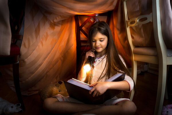 cute girl reading book in self-made house with flashlight