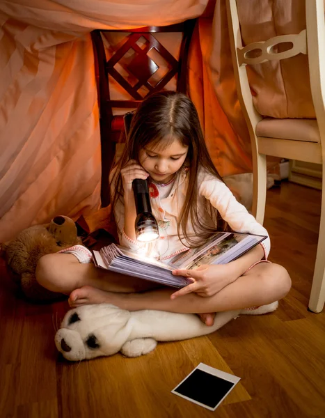 Mädchen sitzt im Schlafzimmer auf dem Boden und liest Buch mit Taschenlampe — Stockfoto