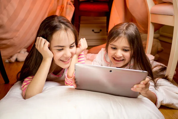 Two happy smiling girls lying on floor and using digital tablet — Stock Photo, Image