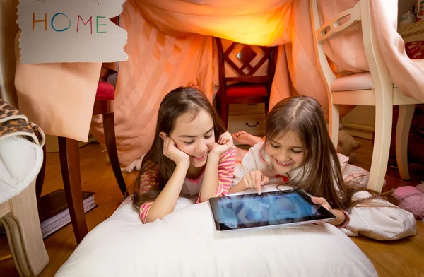 Two girls lying on floor at bedroom and playing on digital table — Stock Photo, Image