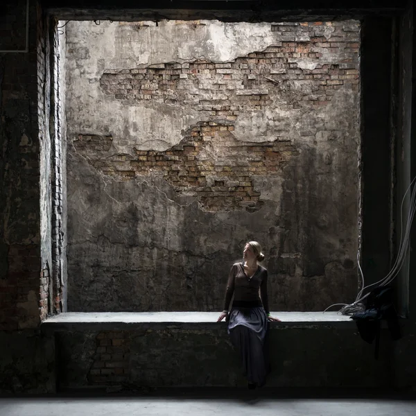 Grungy photo of lonely woman sitting at window in old building — Stock Photo, Image