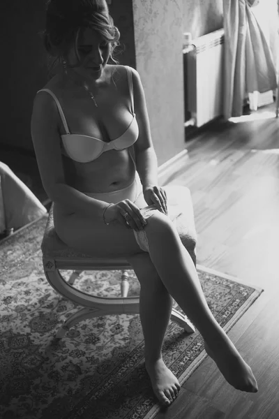 Black and white shot of bride putting on stocking at hotel room — Stock Photo, Image