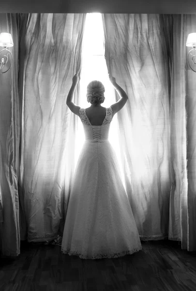 Rear view of elegant bride posing at big window in bedroom — Stock Photo, Image