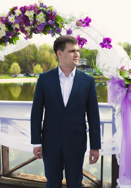 Schöner Bräutigam wartet auf Braut unter Blumenbogen bei Zeremonie — Stockfoto