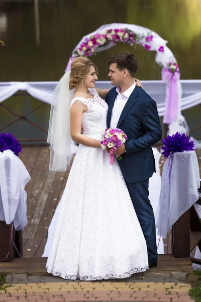 Sorridenti sposi che si guardano sotto arco sul molo — Foto Stock