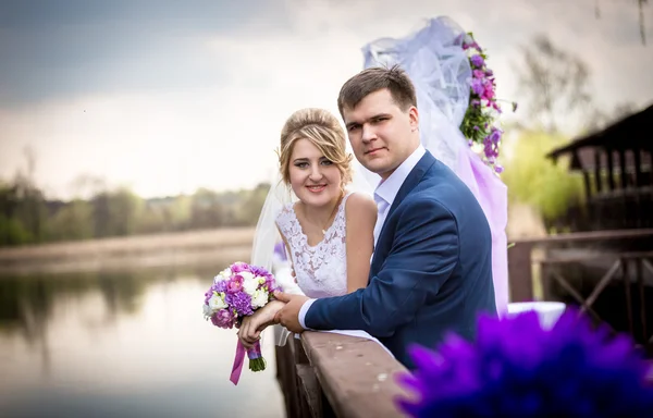 Счастливая невеста и жених позируют на пирсе у озера — стоковое фото
