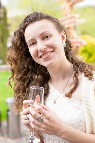 Retrato de mulher encaracolada feliz posando no parque com champanhe — Fotografia de Stock