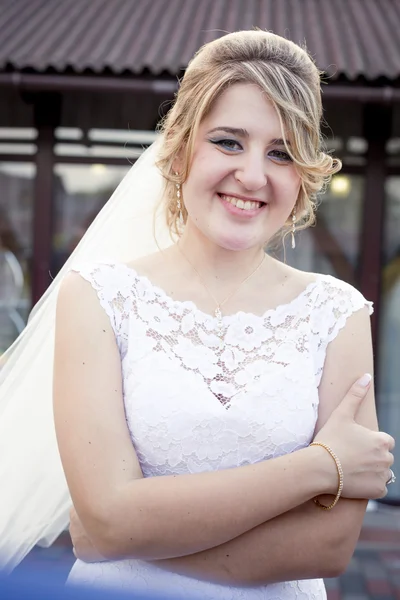 Sonriente rubia novia con largo velo posando al aire libre — Foto de Stock